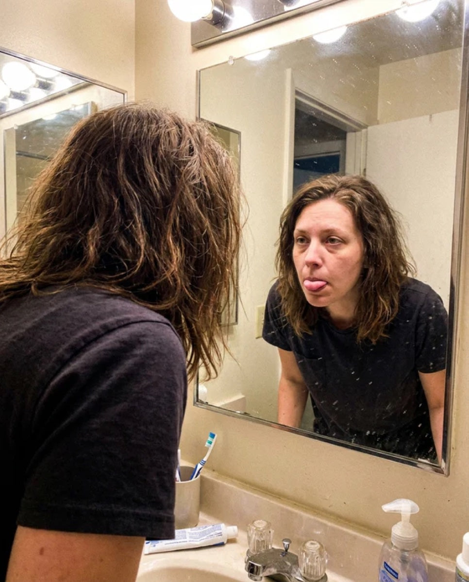 Mujer revisándose la lengua frente al espejo del baño